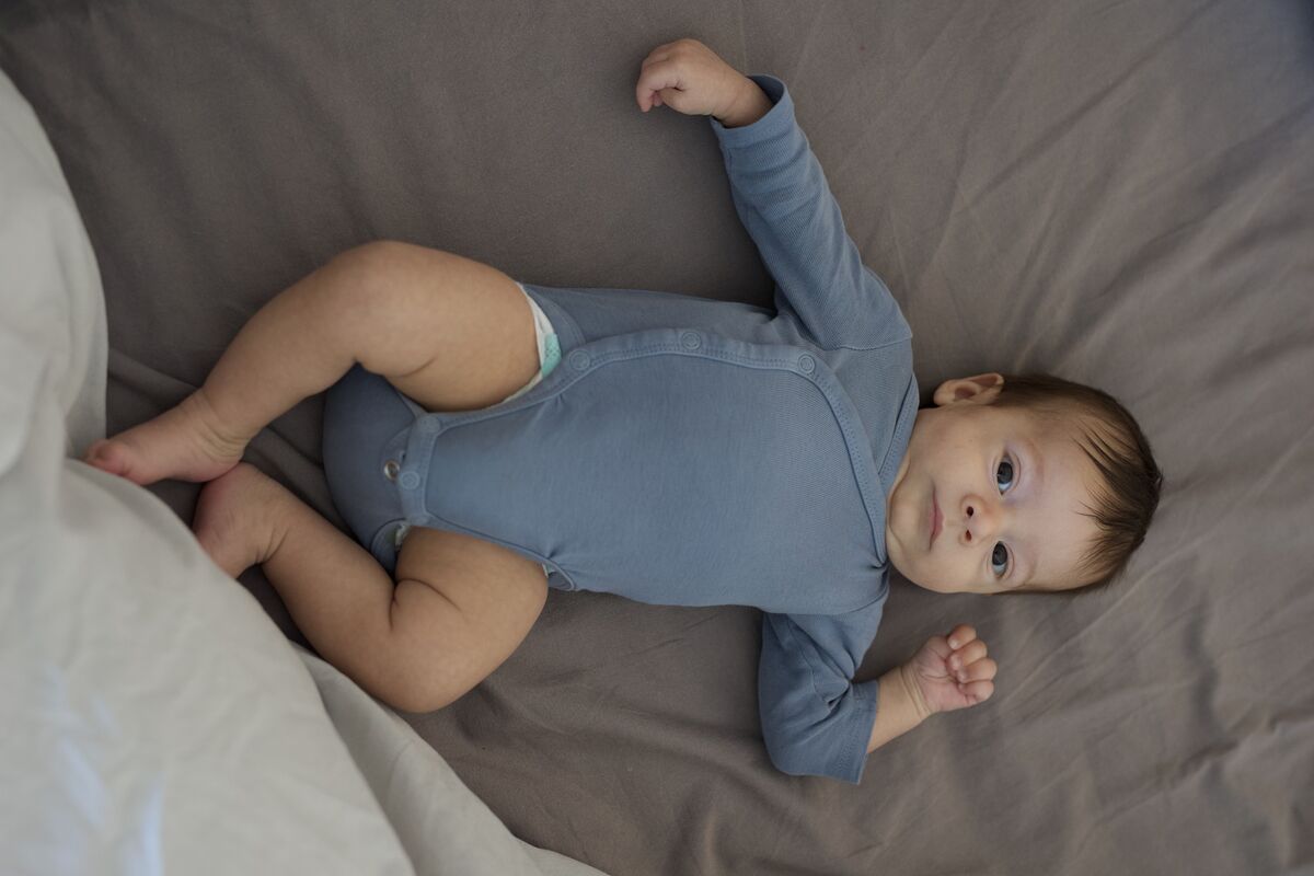 Baby in blue onesie, full body on the bed